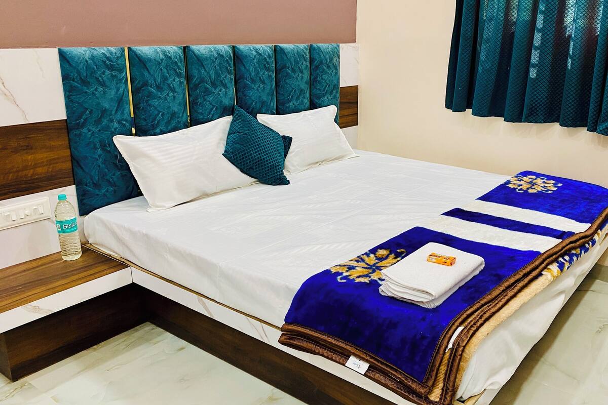 A neatly made bed with a blue and white striped blanket, white pillows, and a water bottle on the nightstand.