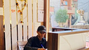 A reception desk with a marble top, a wooden partition with vertical stripes, and a view of the outside through a window. - Hotel Shree Sita Ram Kutti (Ujjain)