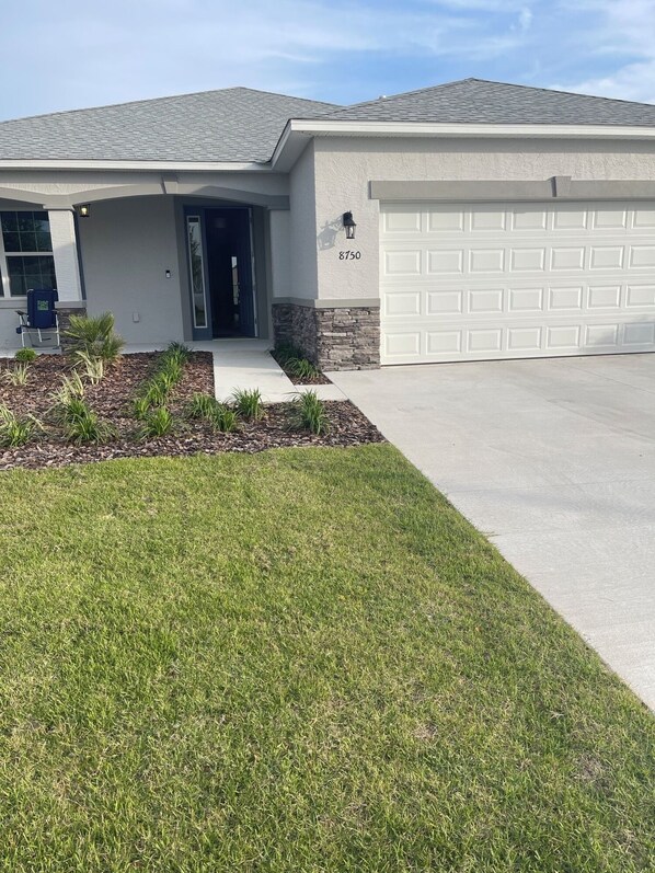 A modern two-story house with a garage, a well-maintained lawn, and a small garden area with plants.