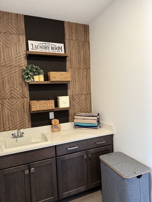 A modern kitchen with a built-in sink, dark cabinets, and a laundry sign above a shelf.