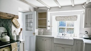 Eine Küche mit weißen Schränken, einem Fenster mit floralem Vorhang und einem Wasserkocher auf der Arbeitsfläche.