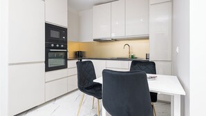 Une cuisine moderne avec des meubles blancs, un micro-ondes noir et une table à manger blanche avec des chaises noires.