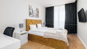 Une chambre d’hôtel avec un lit double, une table de chevet avec une lampe, une chaise, un téléviseur fixé au mur et un tableau au mur.