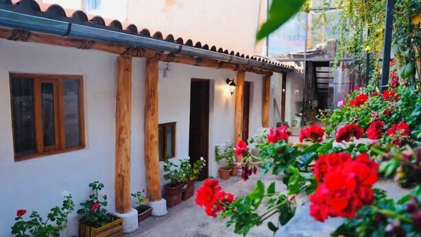 A courtyard with a white building, wooden columns, and potted plants. - Casa tradicional en cusco (Cusco)