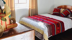 A bedroom with a wooden headboard, a colorful bedspread, and a decorative wooden structure on a nightstand. - Casa tradicional en cusco (Cusco)
