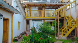 A two-story building with a yellow staircase and a garden with various plants and flowers. - Casa tradicional en cusco (Cusco)