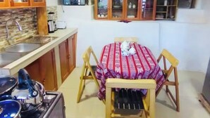 A compact kitchen with wooden cabinets, a gas stove, and a small dining table with a red tablecloth. - Casa tradicional en cusco (Cusco)