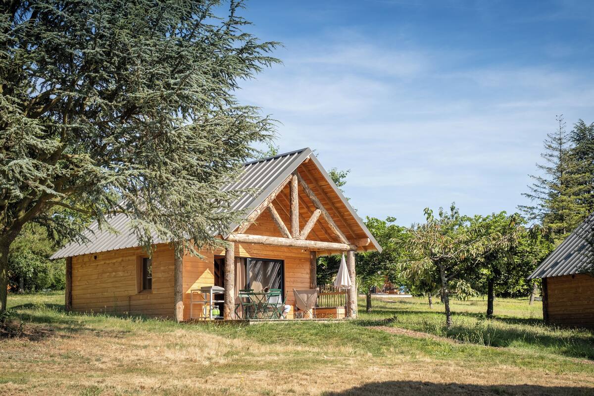 Eine Holzdiele mit Veranda, umgeben von B äumen und Gras.