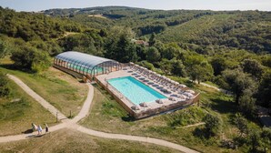 Vista aérea de un resort con una amplia piscina, un área techada y un camino que lleva a la piscina.