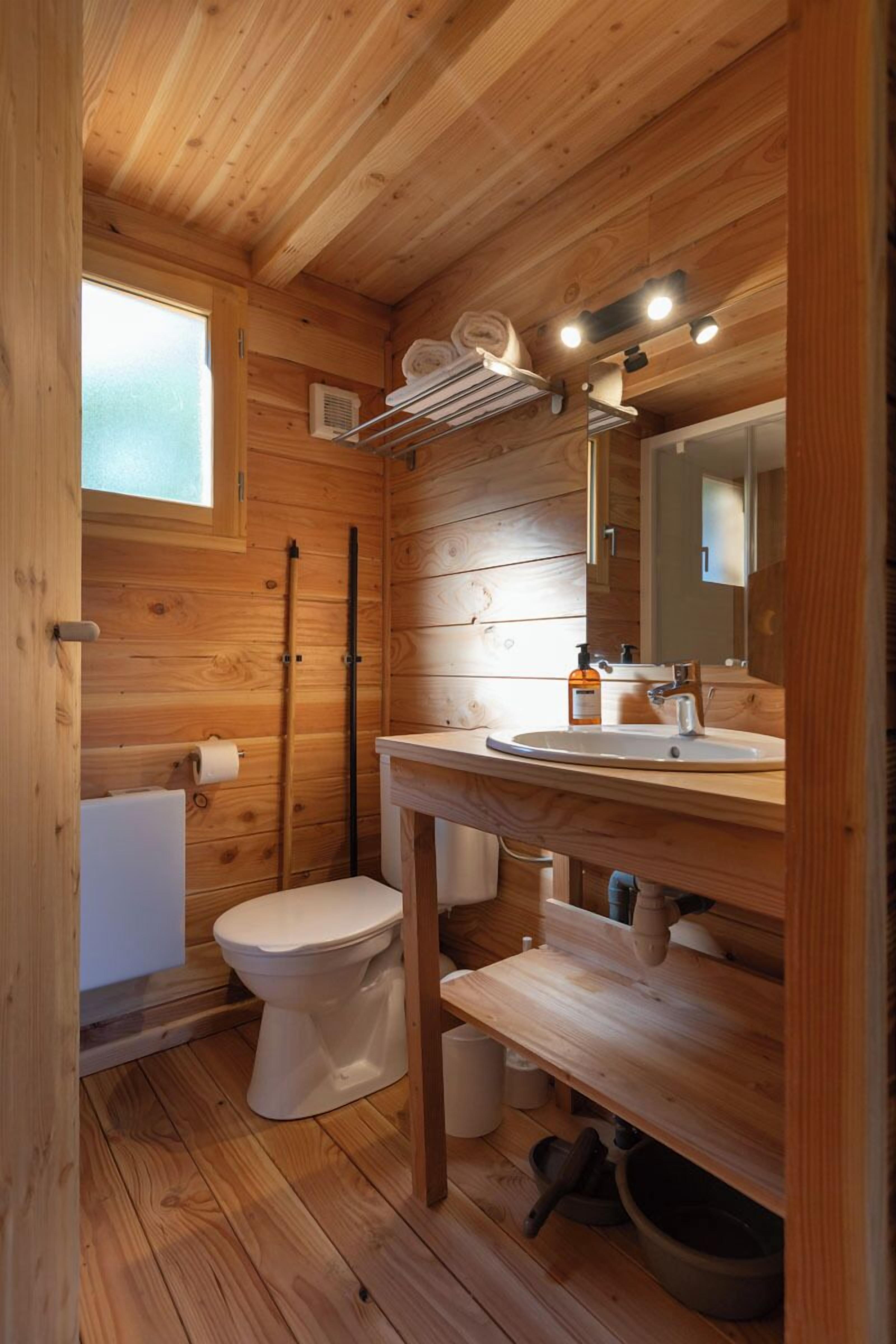 Baño de cabaña de madera con inodoro, lavabo y espejo.