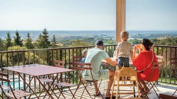 Family enjoys a meal on the outdoor deck with a scenic view of the water and distant hills.