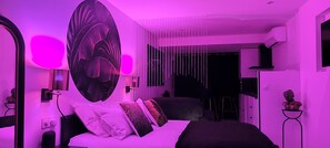 A modern bedroom with a large bed, a wall-mounted artwork, and a ceiling light fixture. - Studio Chic & Terrasse - Cap d'Agde naturist village - Le Boudoir Heliopolis (Cap d'Agde)