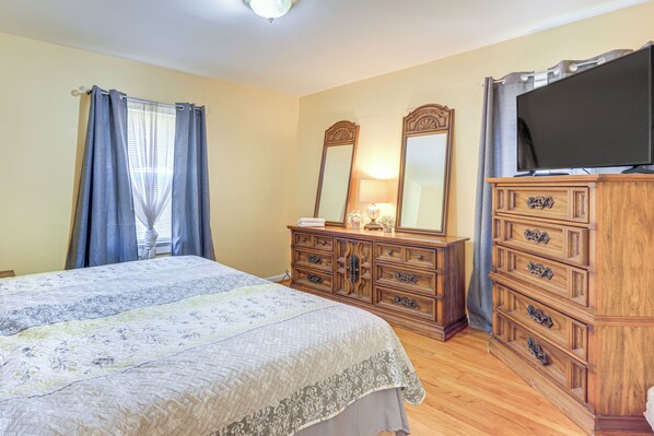 A bedroom with a bed, wooden dresser, and a television.