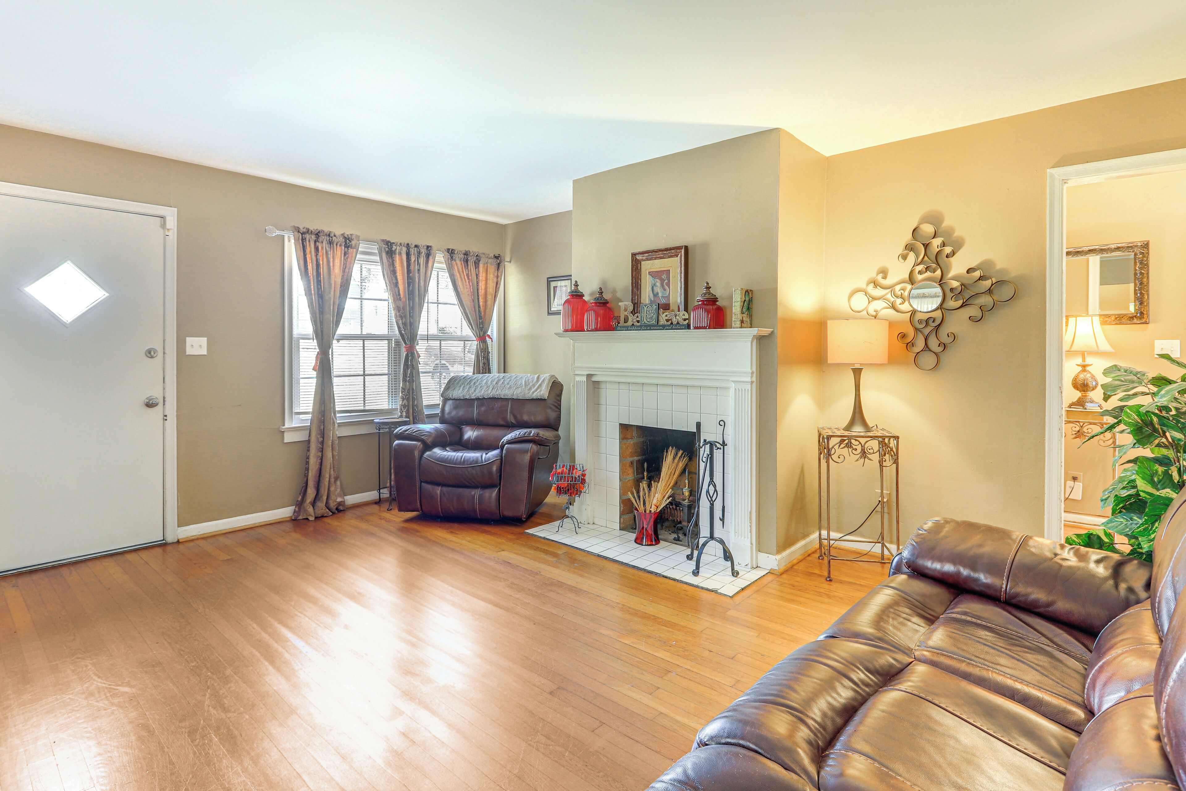 A living room with a fireplace, leather sofa, and a large window with curtains.