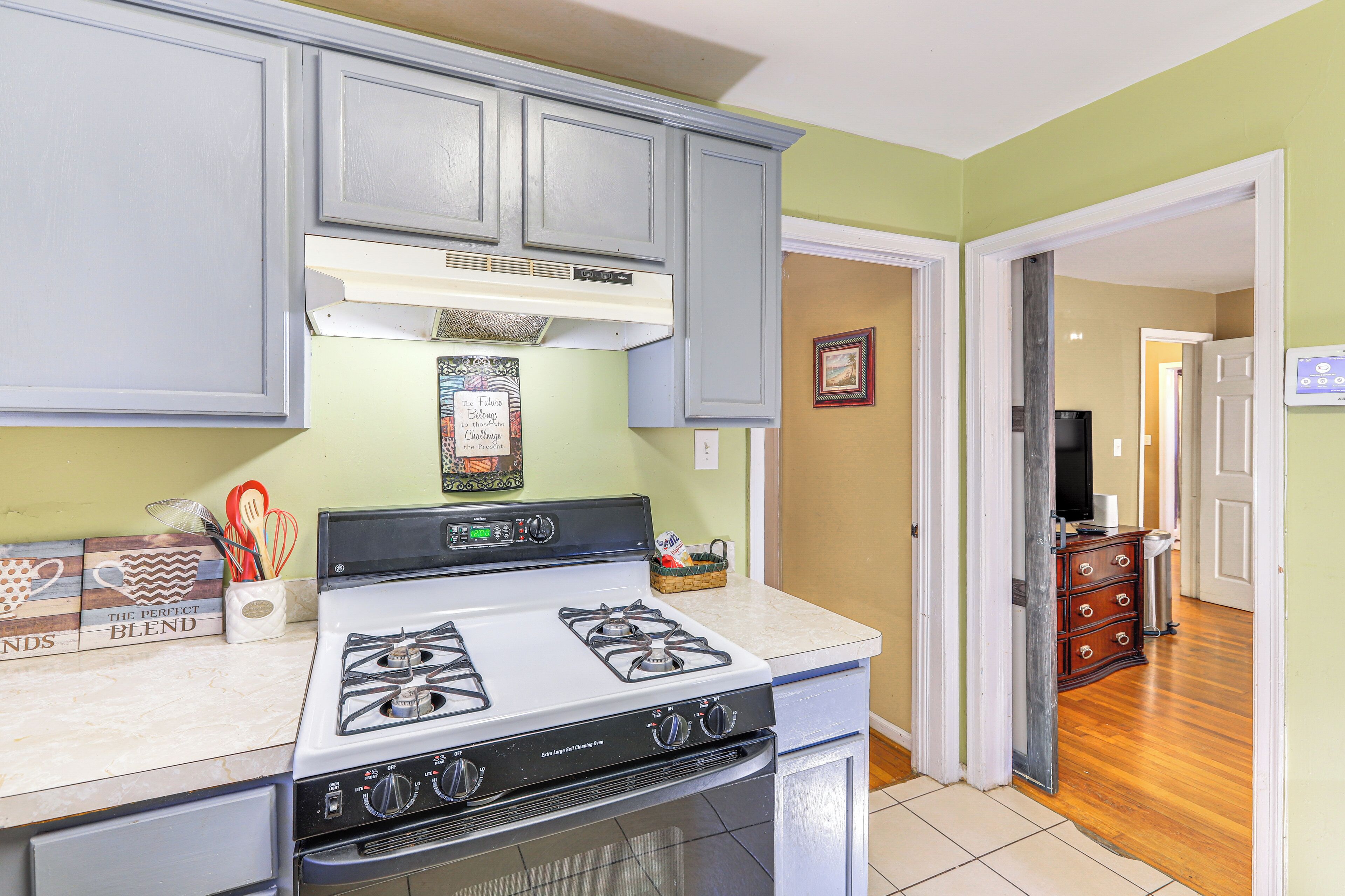 A kitchen with a white stove, grey cabinets, and a tiled floor.
