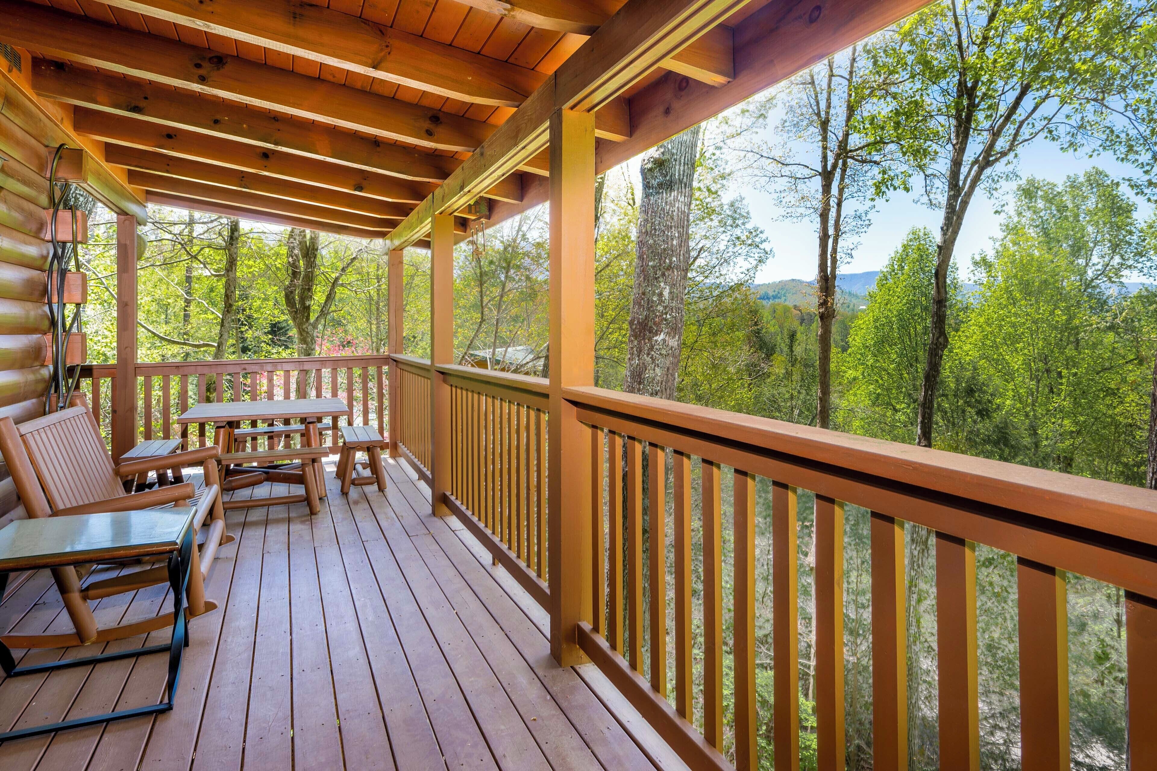 A wooden deck with picnic tables and benches, overlooking a forested area.
