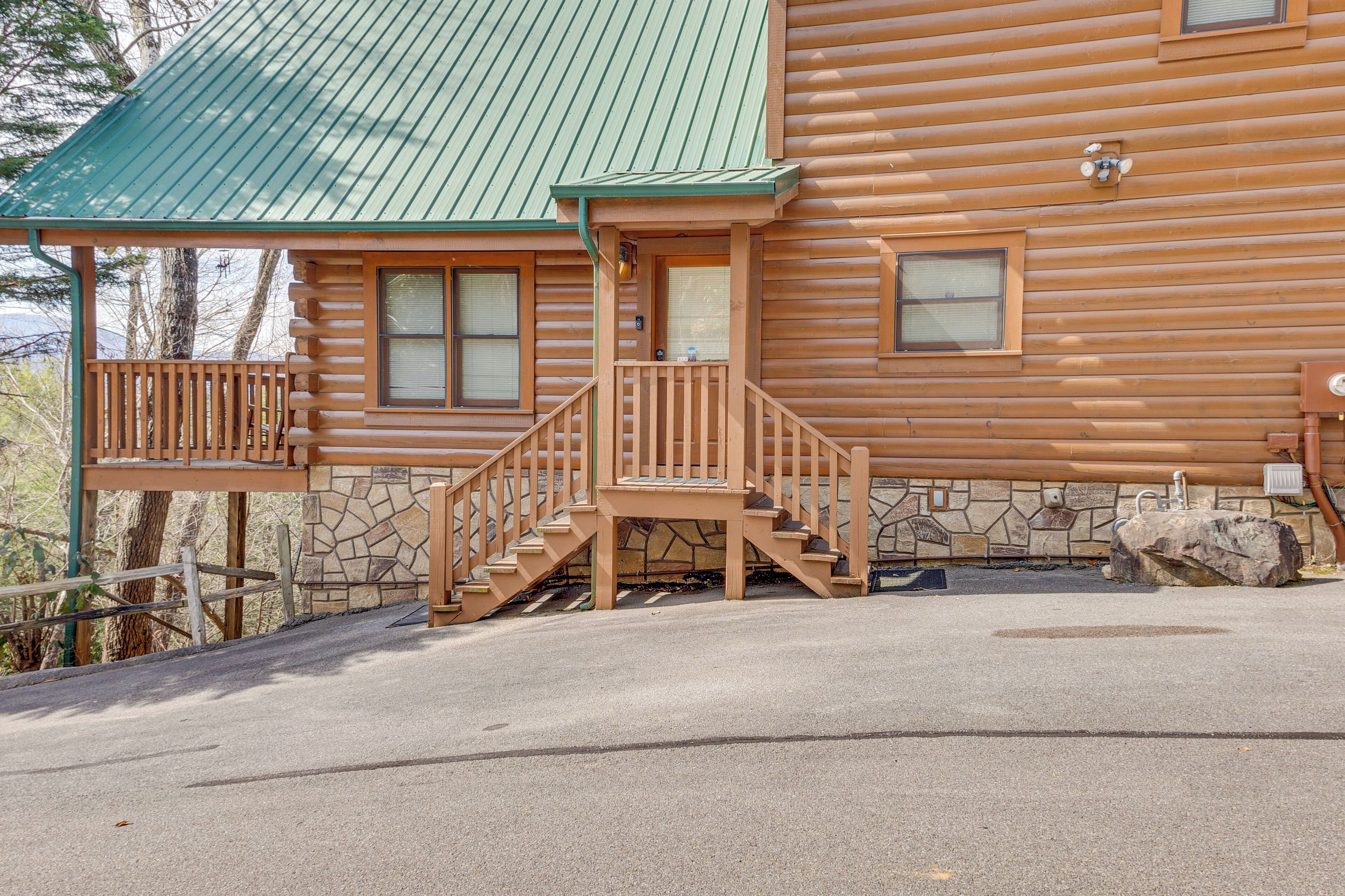 Une cabane en rondins, avec des fondations en pierre, un toit en métal vert et un escalier en bois menant à une véranda.