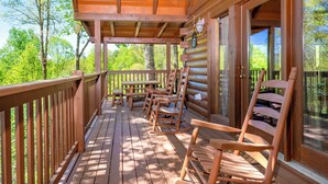 A wooden deck with rocking chairs and a table, overlooking a forested area. - Hot Tub & Game Room: Log Cabin 2 Mi to Ripleys! (Gatlinburg)