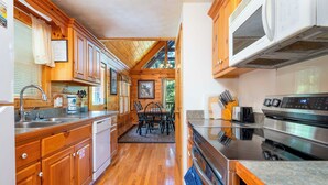 A compact kitchen with wooden cabinets, a stainless steel stove, and a dining area with a table and chairs. - Hot Tub & Game Room: Log Cabin 2 Mi to Ripleys! (Gatlinburg)