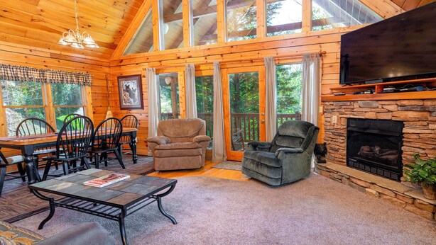 A cozy cabin interior with a stone fireplace, wooden ceiling, and large windows. - Hot Tub & Game Room: Log Cabin 2 Mi to Ripleys! (Gatlinburg)