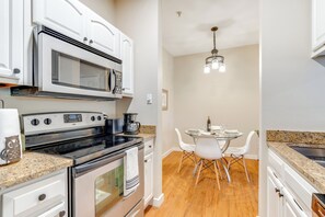 A modern kitchen with white cabinets, a microwave, stove, and granite countertops. There is a dining area with a table and chairs. - 2 Mi to The Domain: Condo w/ Pool & Hot Tub Access (Austin)