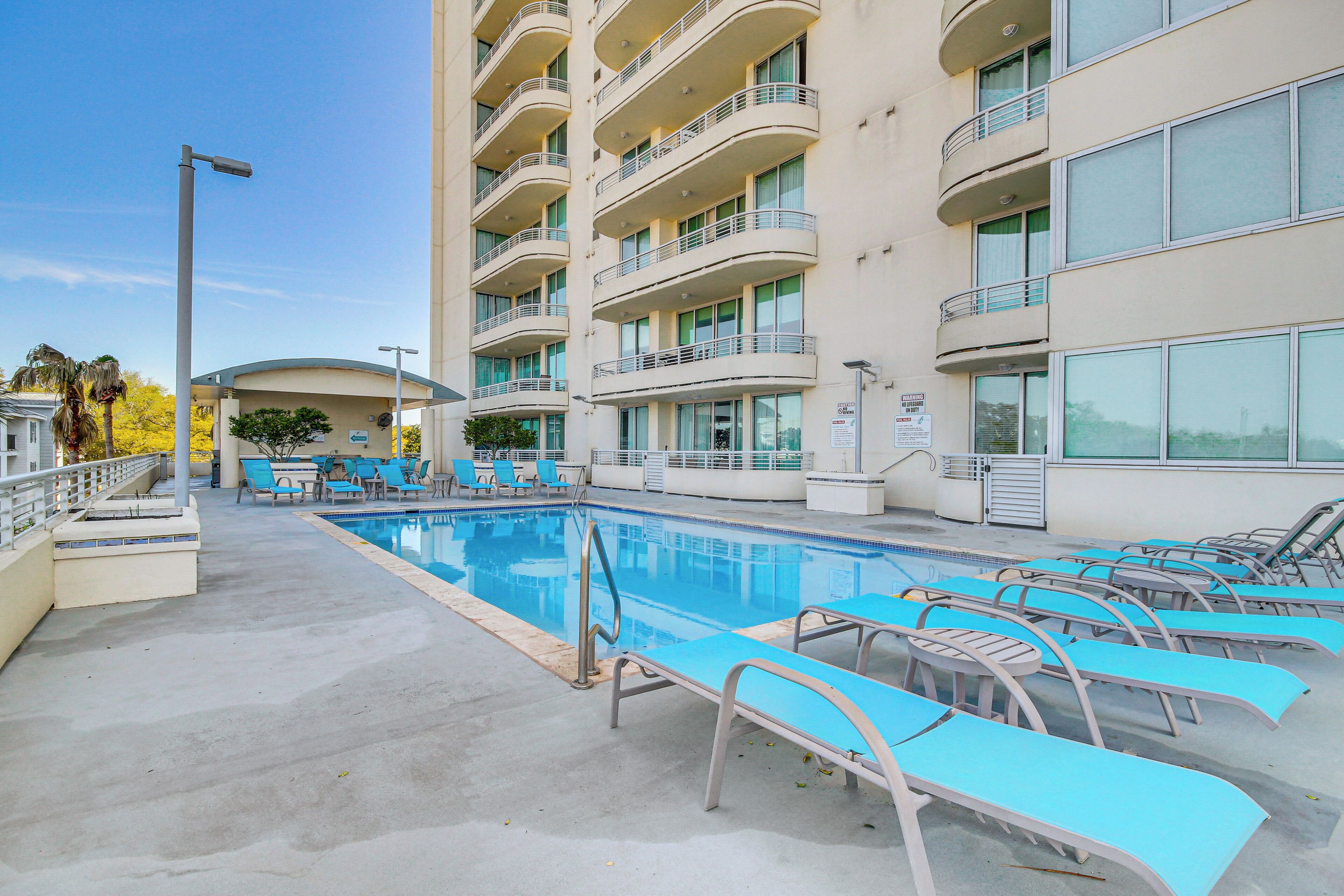 Une piscine avec des chaises longues et un immeuble à plusieurs étages doté de balcons.
