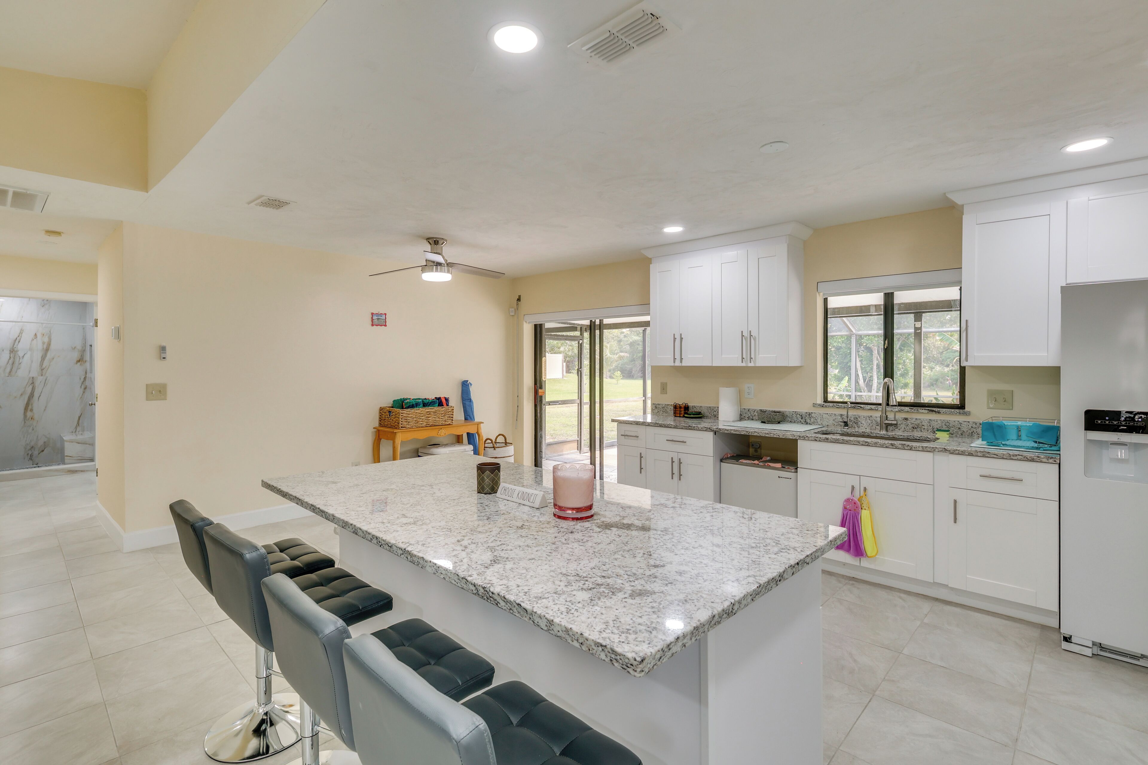 A modern kitchen with white cabinets, a granite countertop, and a bar area with stools.