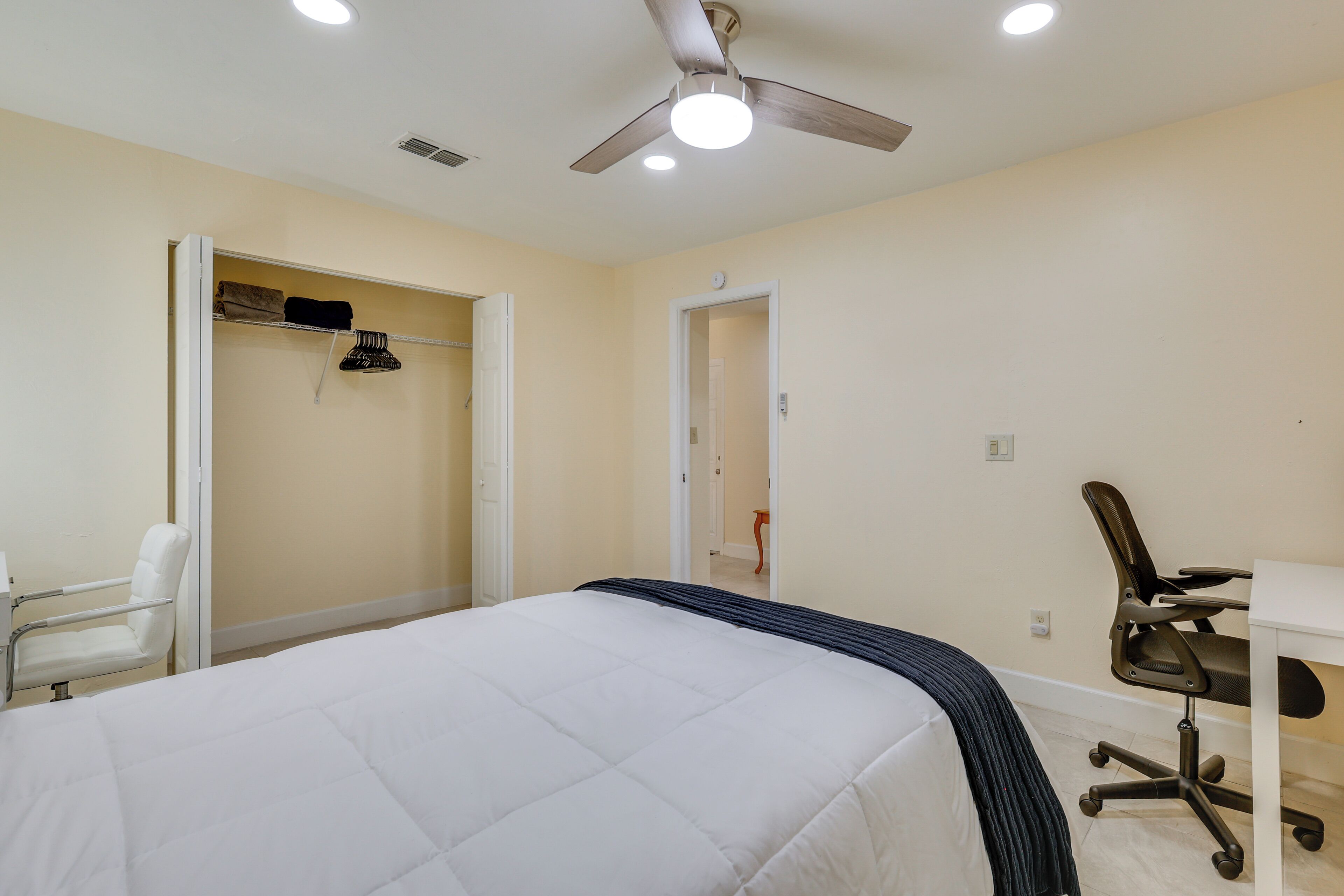 A bedroom with a bed, a chair, a desk, and a ceiling fan.