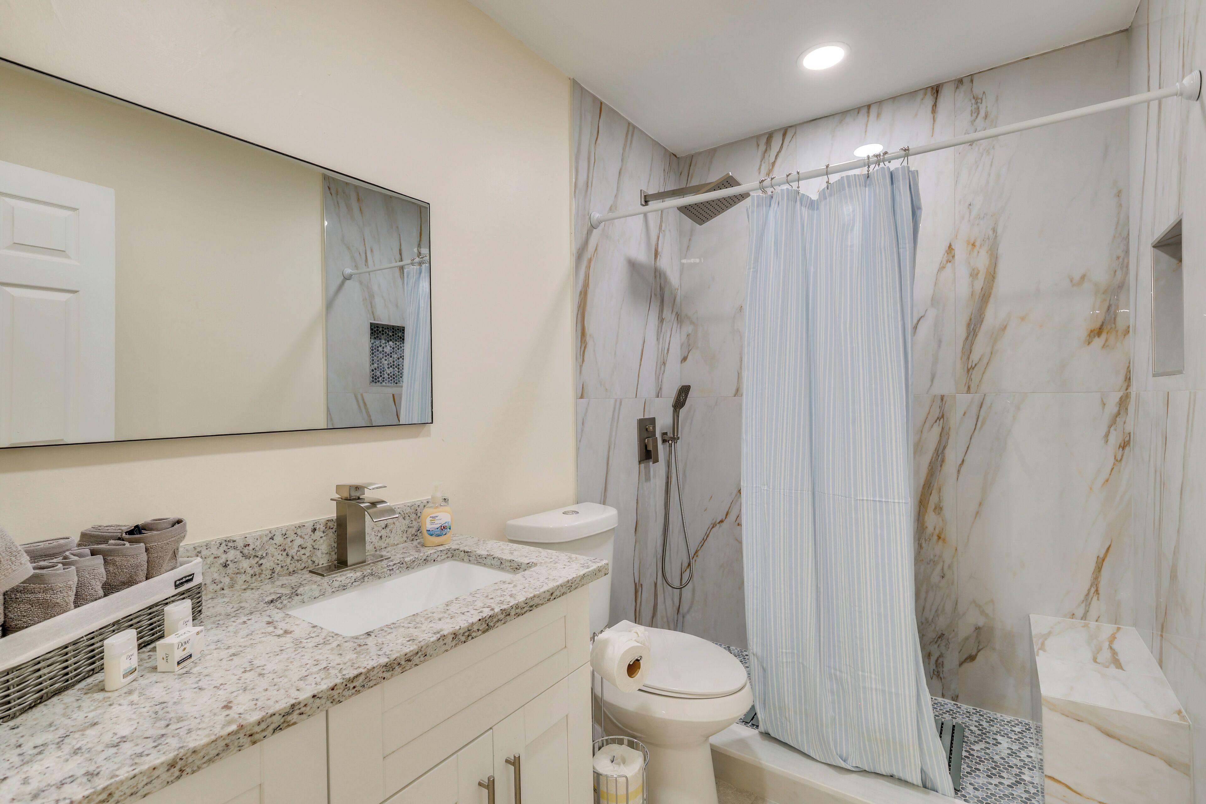 A bathroom with a marble backsplash, a sink, a toilet, and a shower curtain.