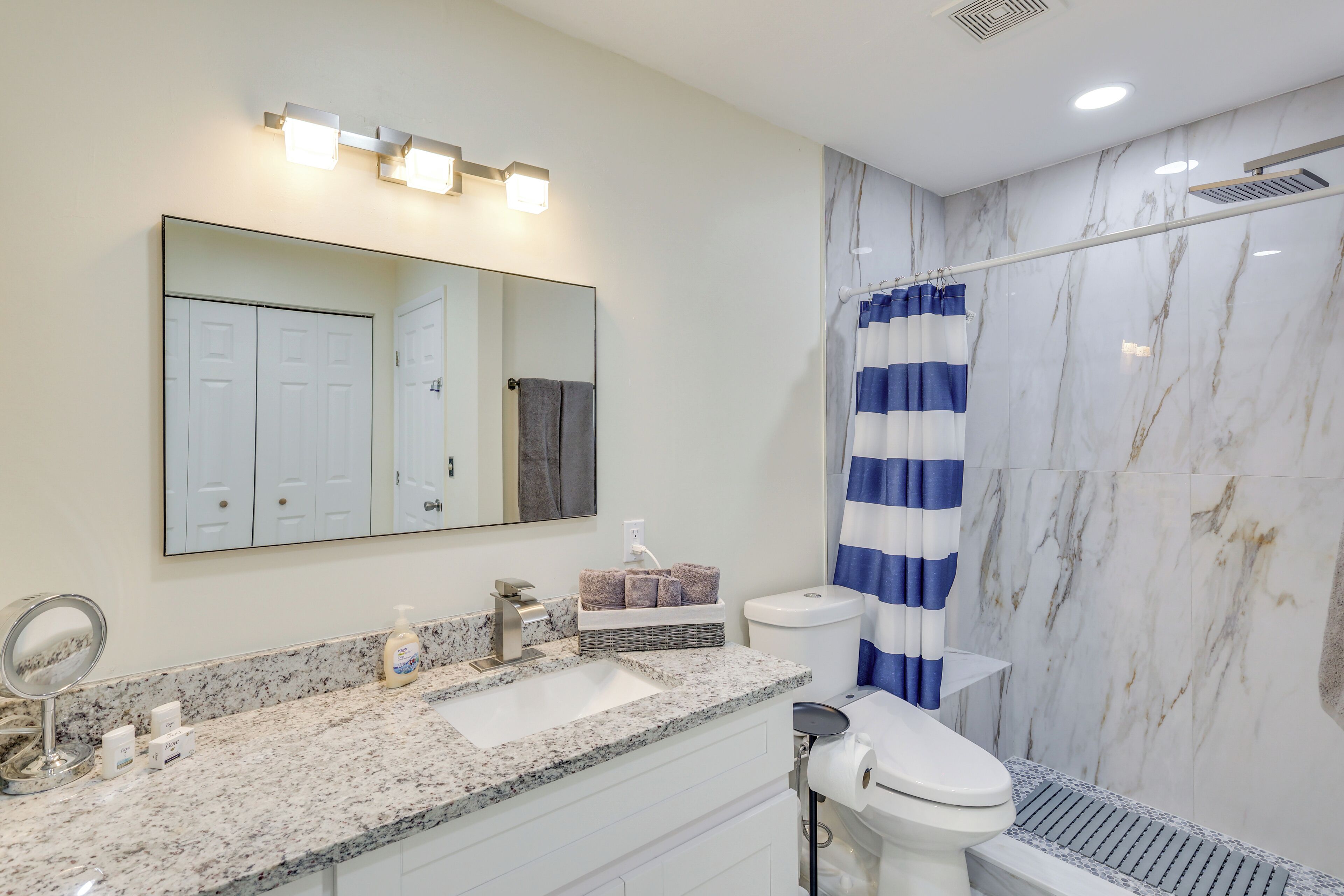 A bathroom with a marble wall, a sink with a mirror, a toilet, and a shower curtain.