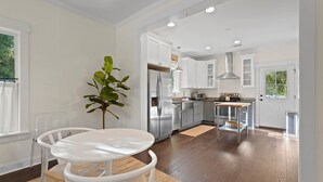 Una cocina moderna con armarios blancos, electrodomésticos de acero inoxidable y una zona de comedor con mesa y sillas blancas.