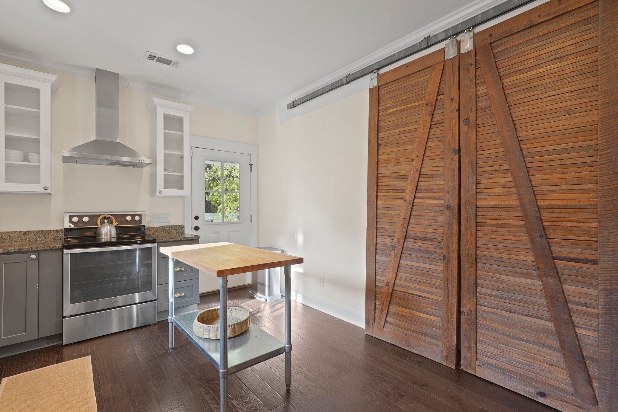 Une cuisine équipée d’appareils électroménagers en acier inoxydable, avec une table en bois et une porte coulissante de style rustique.