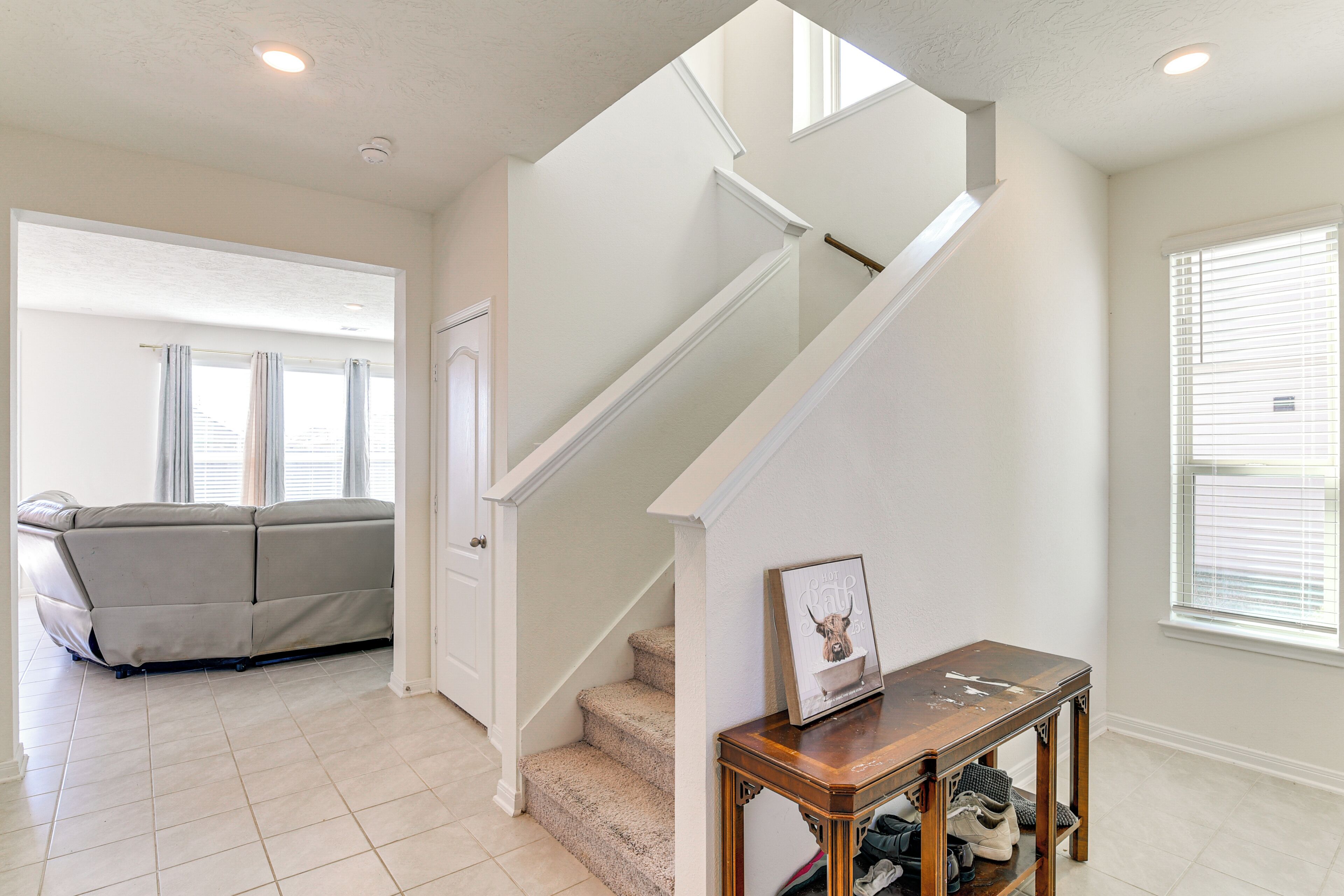 A living room with a beige sofa, a wooden console table, and a staircase with white railings.