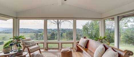 A sunroom with a wooden bench, chairs, and a ceiling fan.