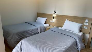Habitación de hotel con dos camas individuales, cada una con cabecera de madera y mesita de noche. Hay un aplique en la pared sobre las camas.