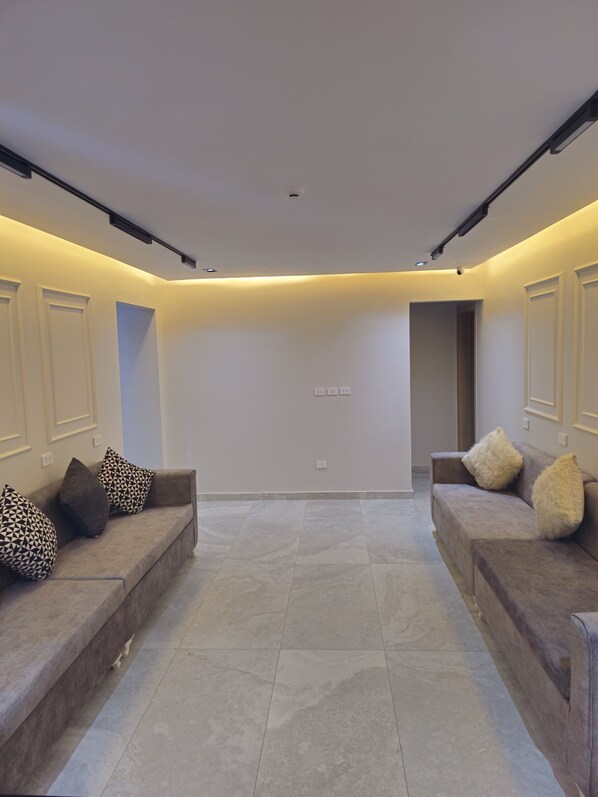 Un salon moderne avec deux canapés, un sol carrelé, des spots encastrés au plafond et un mur sobre agrémenté d’une porte.