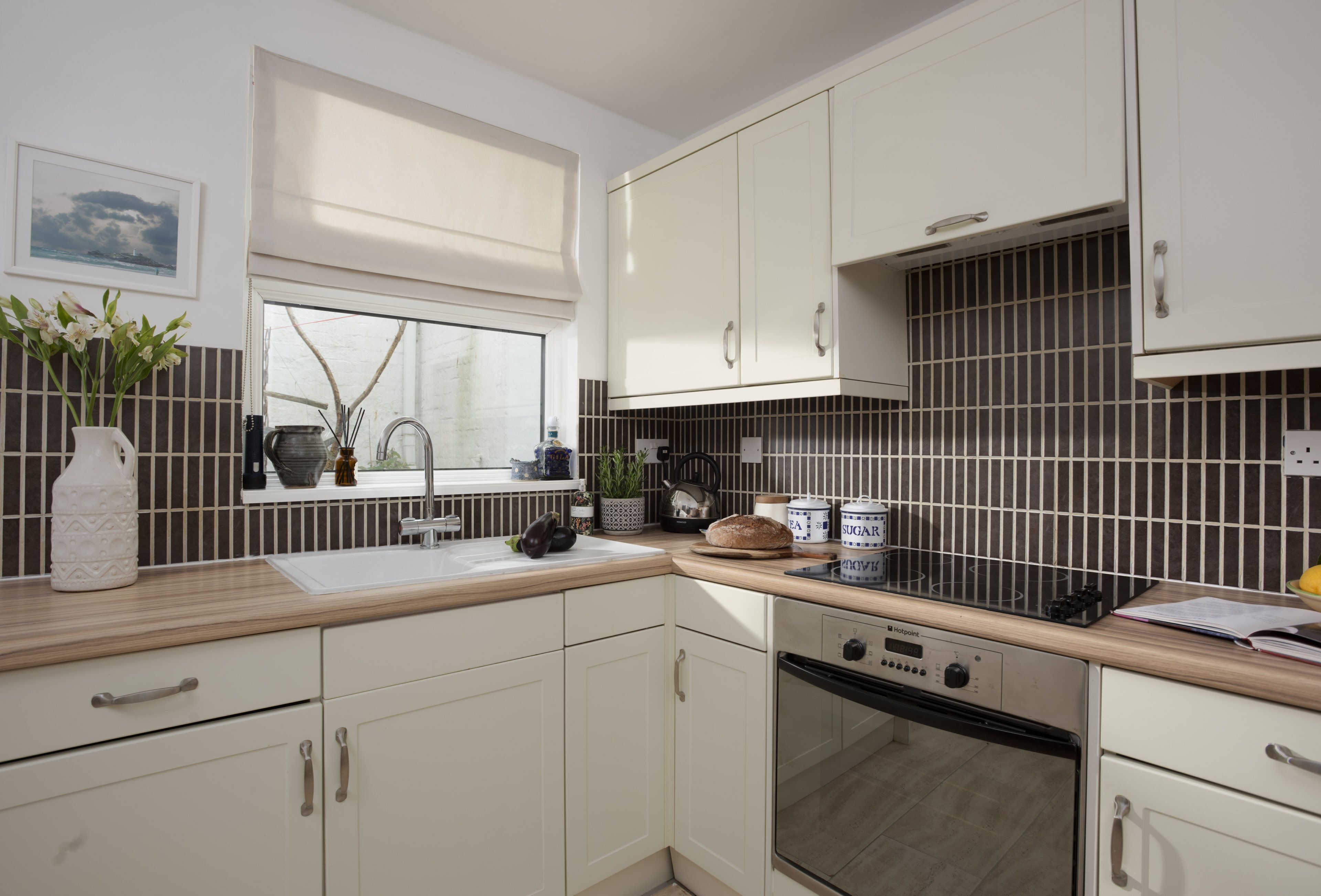A modern kitchen with white cabinetry, a window with a view, and a black tiled backsplash.
