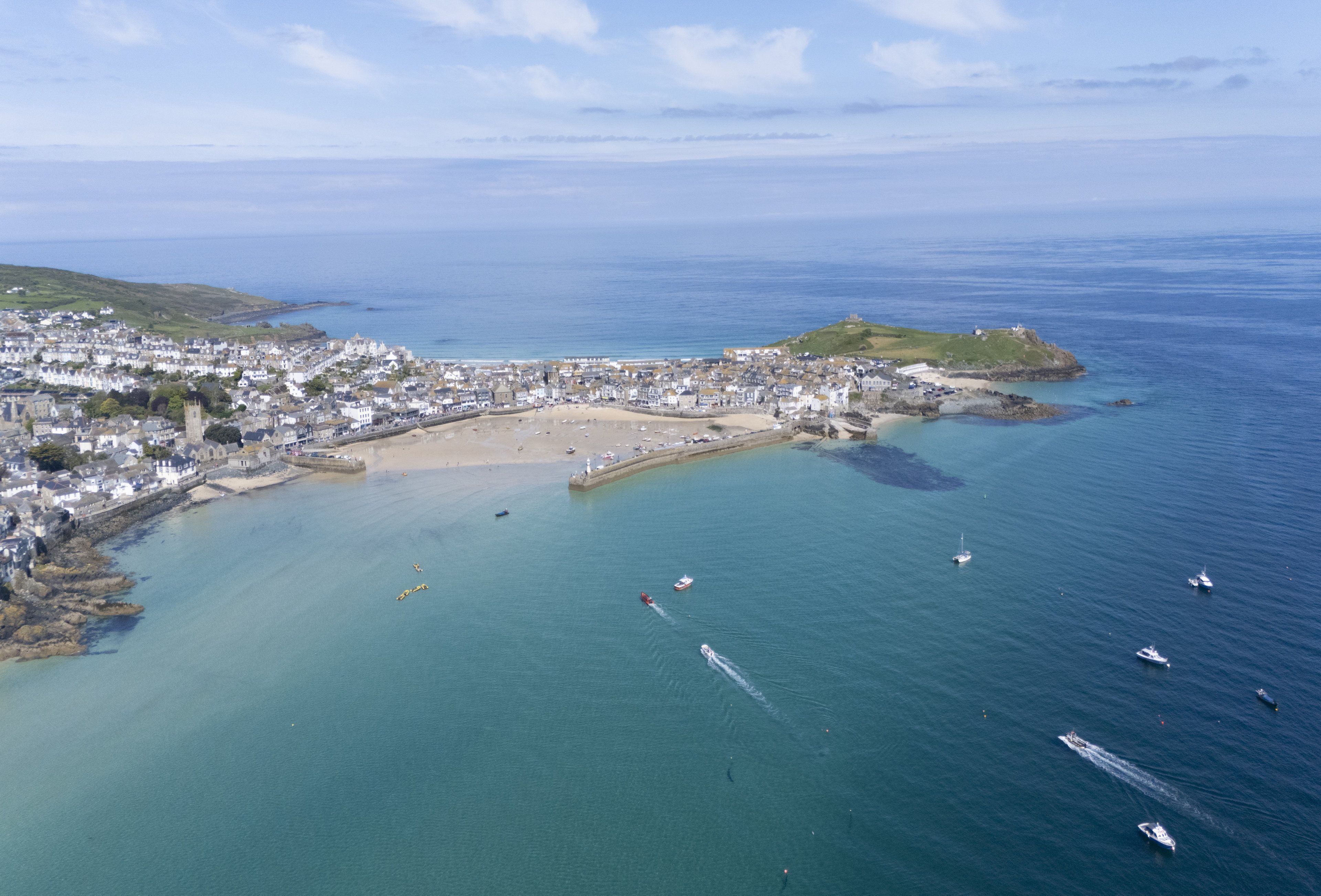 An aerial view of a coastal town with a beach, boats, and a lighthouse.