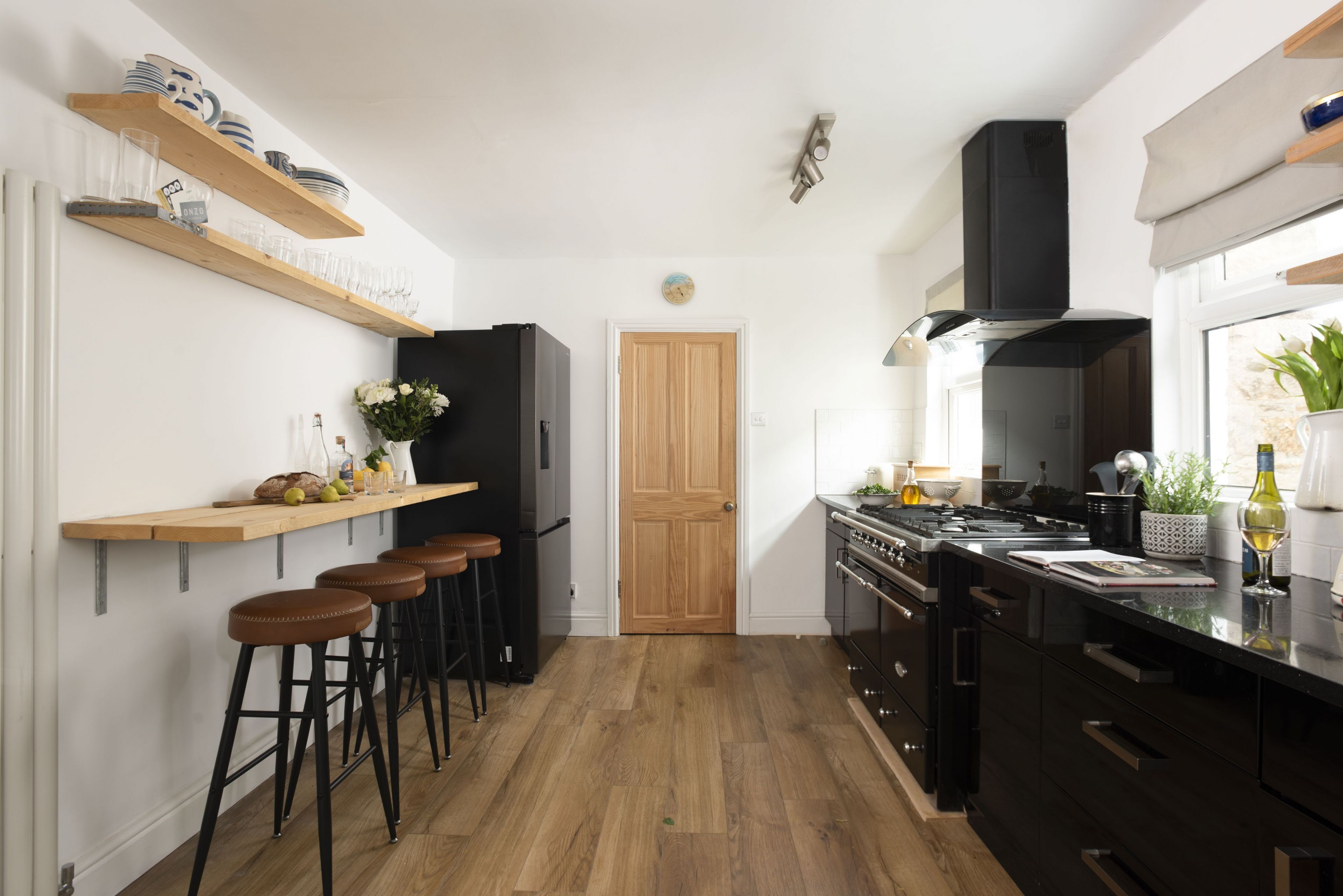 Una cocina moderna con un refrigerador negro, taburetes de bar de madera y una puerta de madera.