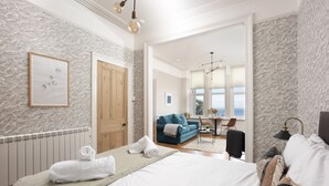 Ett hotellrum med en stor säng, en blå soffa, ett matbord med stolar och utsikt över havet genom fönstren.