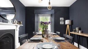 Ett matrum med ett träbord dukat för fyra personer, omgivet av svarta stolar, en vas med blommor och en lampa på ett sidobord.