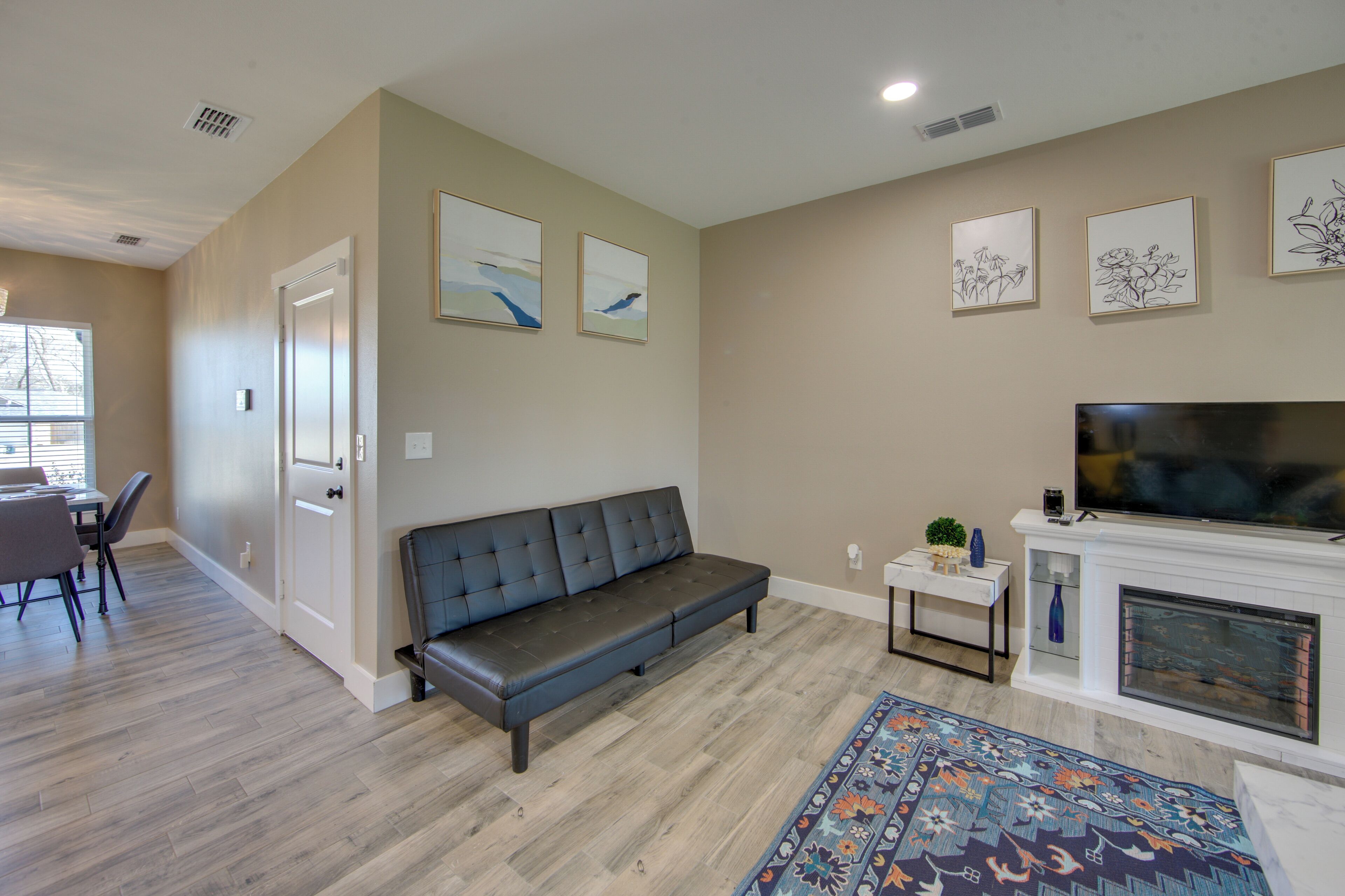 A modern living room with a grey sofa, a flat-screen TV, a fireplace, and a dining area with a table and chairs.