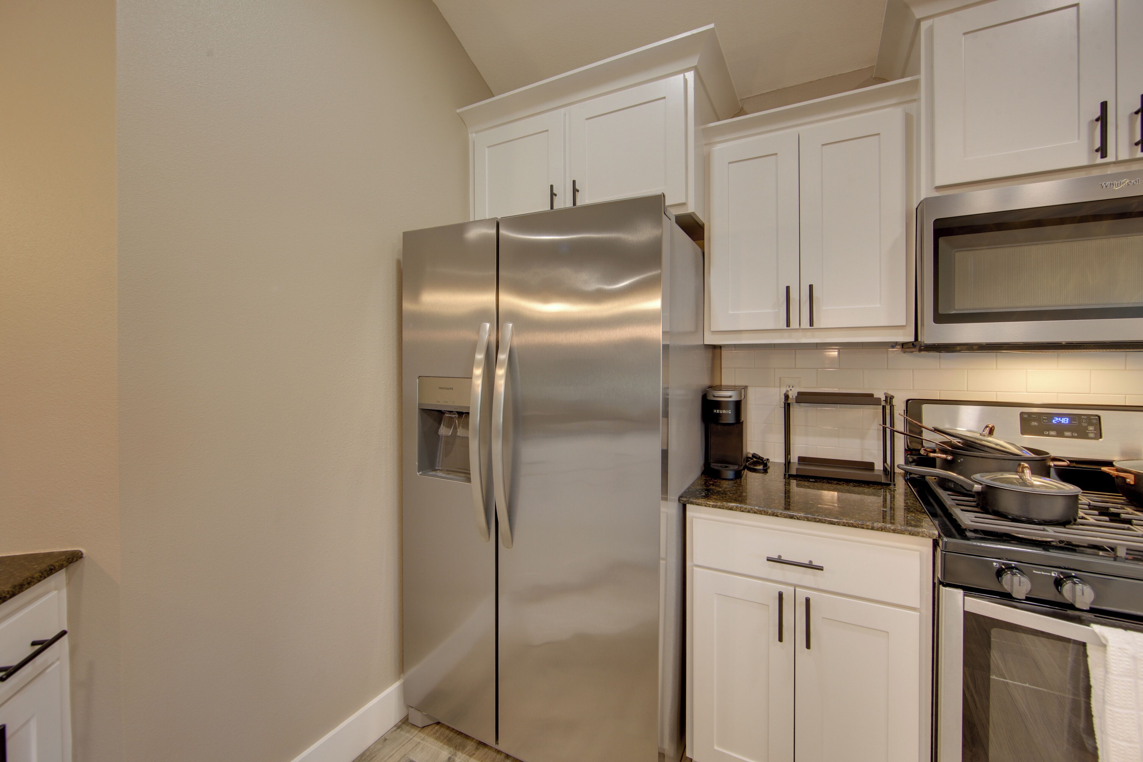 Una cocina con un refrigerador de acero inoxidable, un microondas, una estufa y armarios blancos.