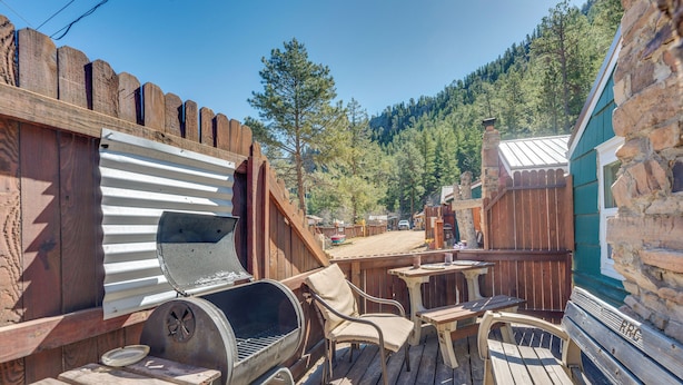 Een houten terras met een barbecue, stoelen en een tafel.