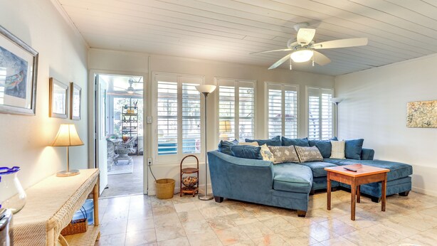A living room with a blue sofa, a wooden coffee table, wicker furniture, and a ceiling fan. - Englewood Bungalow 1 Mi to Beach: Pets Welcome! (Englewood)