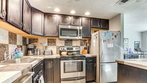 A modern kitchen with dark wooden cabinets, stainless steel appliances, and a marble backsplash. - Englewood Bungalow 1 Mi to Beach: Pets Welcome! (Englewood)