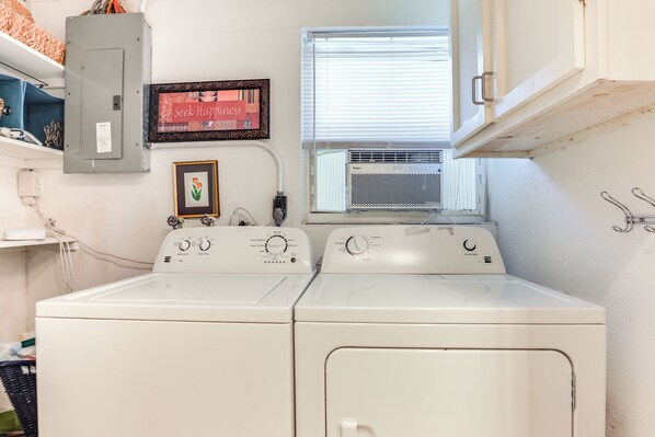 A laundry area with two front-loading washers and dryers, a window with blinds, a framed motivational quote, and a utility meter. - Englewood Bungalow 1 Mi to Beach: Pets Welcome! (Englewood)