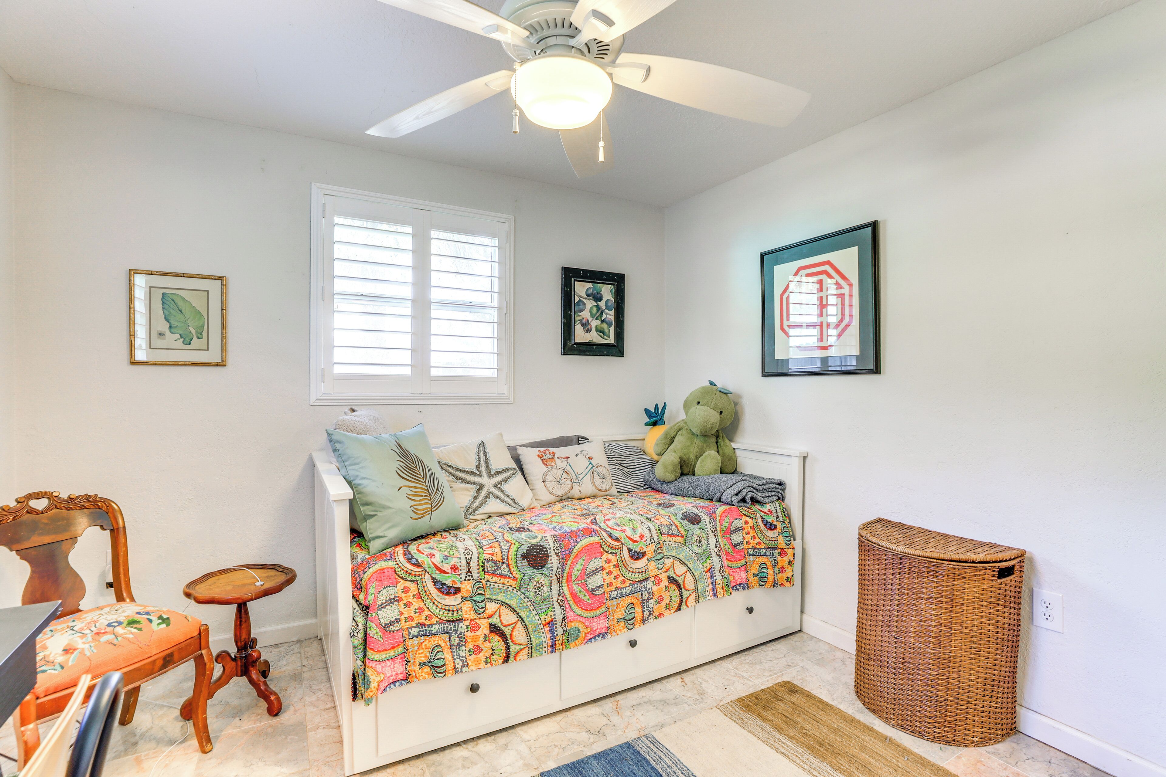 A bedroom with a bed, a ceiling fan, a window, and a wall-mounted trash can.
