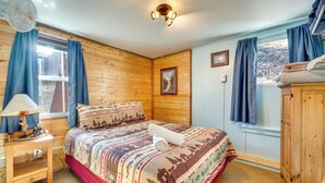 A cozy bedroom with a wooden headboard, a bed with a patterned bedspread, a bedside table with a lamp, and a window with curtains. - Fish, Hike & Unwind: Drake Cabin w/ Hot Tub! (Drake)