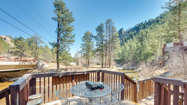 A wooden deck with a round metal table and chairs, overlooking a forested area and a river. - Fish, Hike & Unwind: Drake Cabin w/ Hot Tub! (Drake)